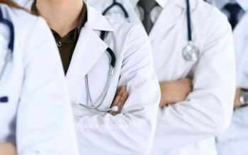 Three doctors wearing white coats stand in a line with their arms crossed.