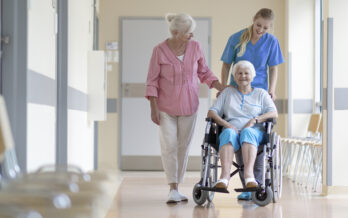 Two elderly women being escorted through hospital