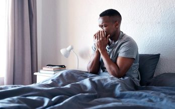 Young man sick in bed blows his nose