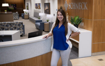 Brieanne Jungels smiles while standing at the Schneck reception desk, with the lobby visible behind her.