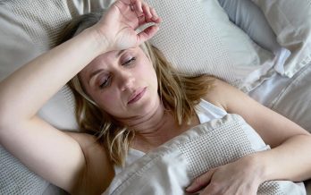 Lady lays in bed with her arm across her forehead, exasperated