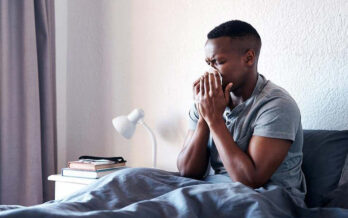 Young man sits in bed, unwell, blowing his nose