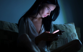 Woman stares at her phone in a dark room