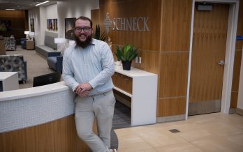 Tucker Brush stands and smiles in the Schneck reception area, leaning casually on the front desk.