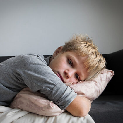 Picture of little boy looking sad laying down holding a pillow