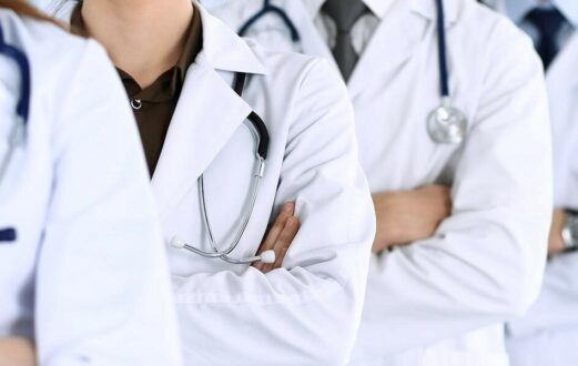Three doctors wearing white coats stand in a line with their arms crossed.