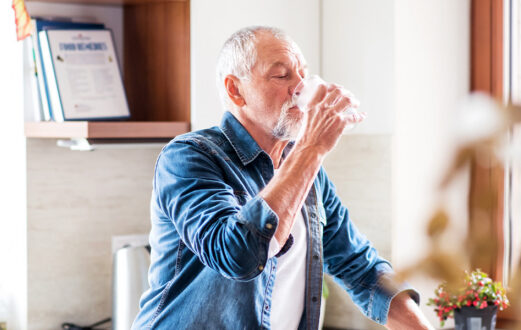 An older man in a blue button down drinking a glass of water
