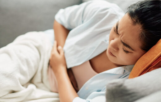 A woman clutching her abdomen and grimacing in pain while laying on her side