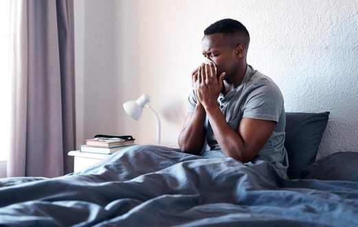 Young man sick in bed blows his nose