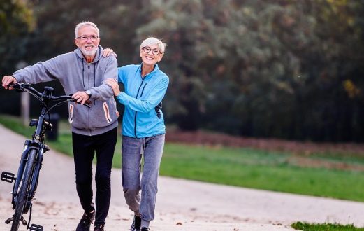 Elderly couple walk along side their bike on a paved biking trail