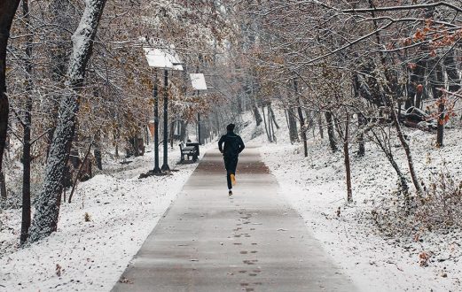 Person runs on a snow covered walking trail in the winter