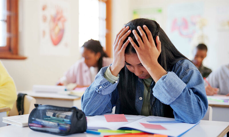 Picture of a girl stressed at school with hands on her head looking down