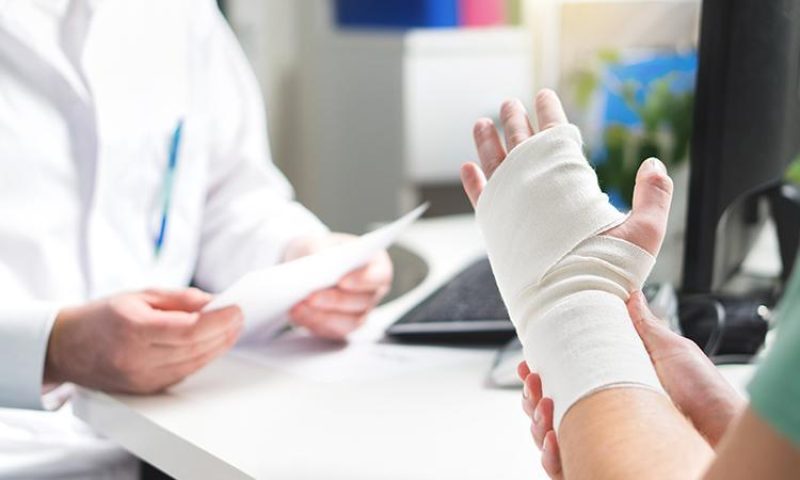 Doctor holding papers while a patient with a bandaged hand gestures during a consultation.