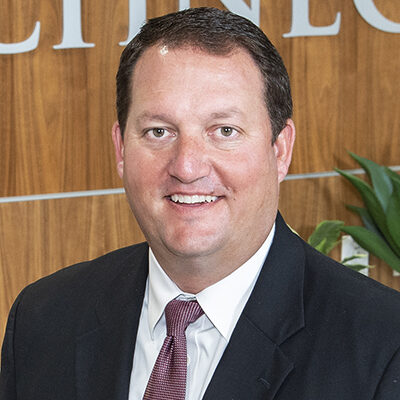 Close up photo of Eric Fish, Schneck President & CEO. He is smiling, has dark hair and is wearing a dark suit.
