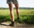 Close up of person's legs who is wearing shorts, as they step of a trail and into a grassy field