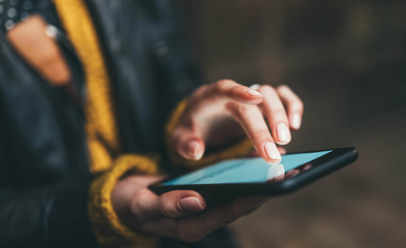 A woman views her cellphone. Her manicured fingers touch the screen, reading the information.