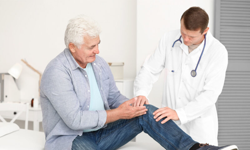 older man talking to doctor while holding knee
