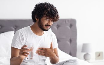 man holding his chest with one hand and a glass of water in the other