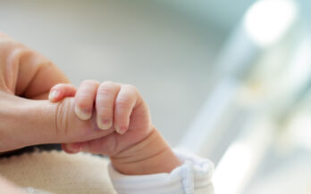 newborn holding mother's thumb