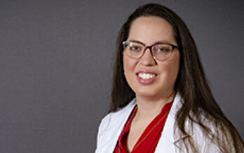Dr. Kristin Sanders is pictured in a red dress on a gray backdrop