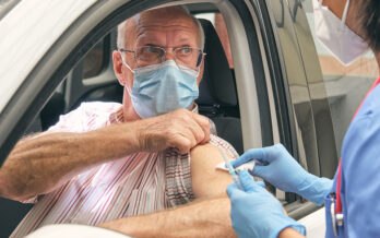 Older man pulls up sleeve while sitting in his car as nurse prepares to give him a vaccine