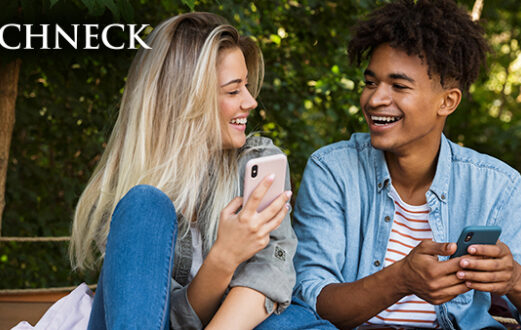 two older teens, a boy and a girl, laugh while looking at their phones together