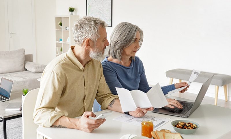 Photo of a couple sitting at a table with a computer and papers