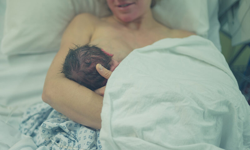 Close up of newborn breastfeeding while being held by his mother right after birth