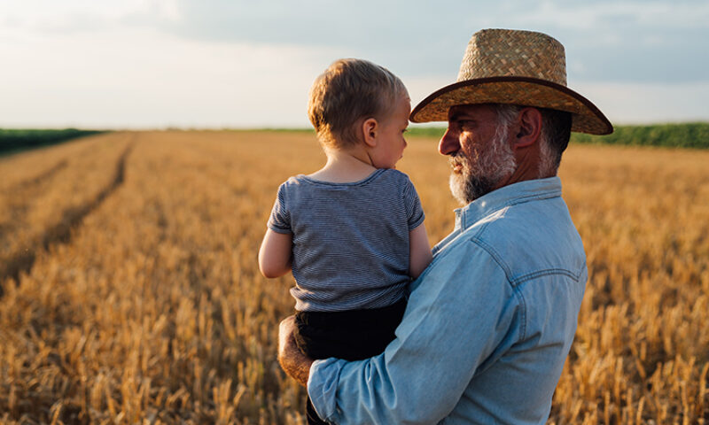 farmer holding a baby in front of farm